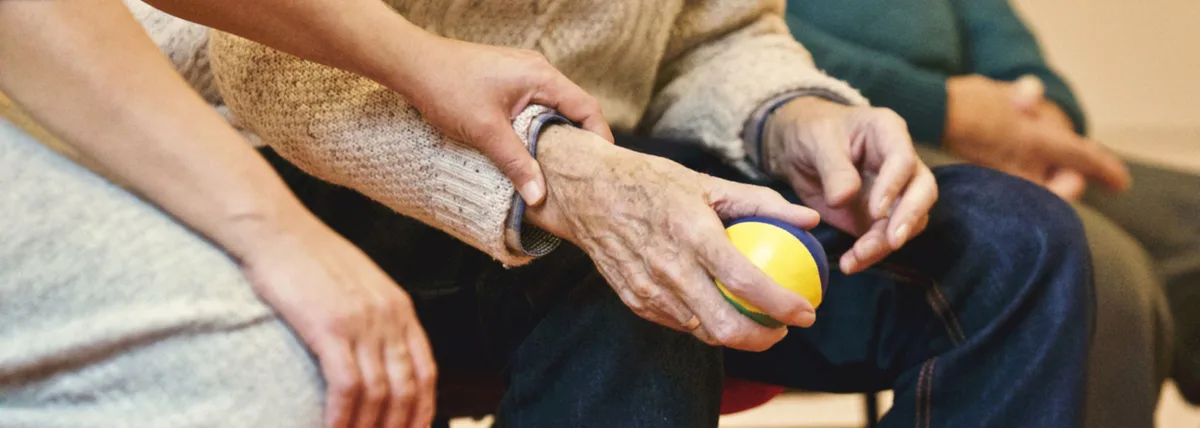 Hände zweier Menschen, eine ältere Person hält einen Ball